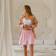 Load image into Gallery viewer, Woman in colorful shirt and pink shorts standing in a stylish room with white decor.