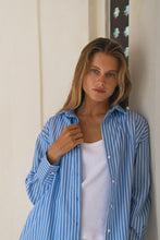 Load image into Gallery viewer, Woman wearing a blue striped shirt over a white top against a neutral wall.