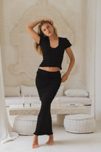 Load image into Gallery viewer, Woman in black shirred top and shirred maxi skirt standing in a minimalistic room with white decor