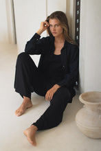 Load image into Gallery viewer, Woman wearing a black outfit sitting on a white floor with a vase in the background