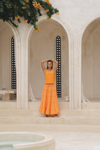 Load image into Gallery viewer, Woman in an orange skirt and tank top standing in front of a classical architectural archway in a marble courtyard.