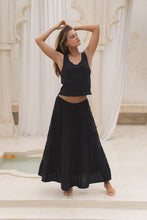 Load image into Gallery viewer, Woman in a black tank top and skirt  standing on steps with white columns in the background