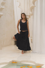Load image into Gallery viewer, Woman in a black tank top and skirt  standing on steps with white columns in the background