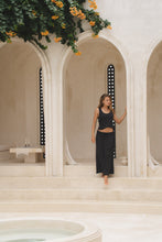 Load image into Gallery viewer, Woman wearing a black maxi skirt and tank top in front of a decorative archway.
