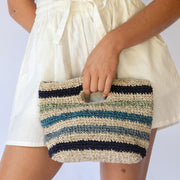 Person holding a striped woven clutch bag against a plain background