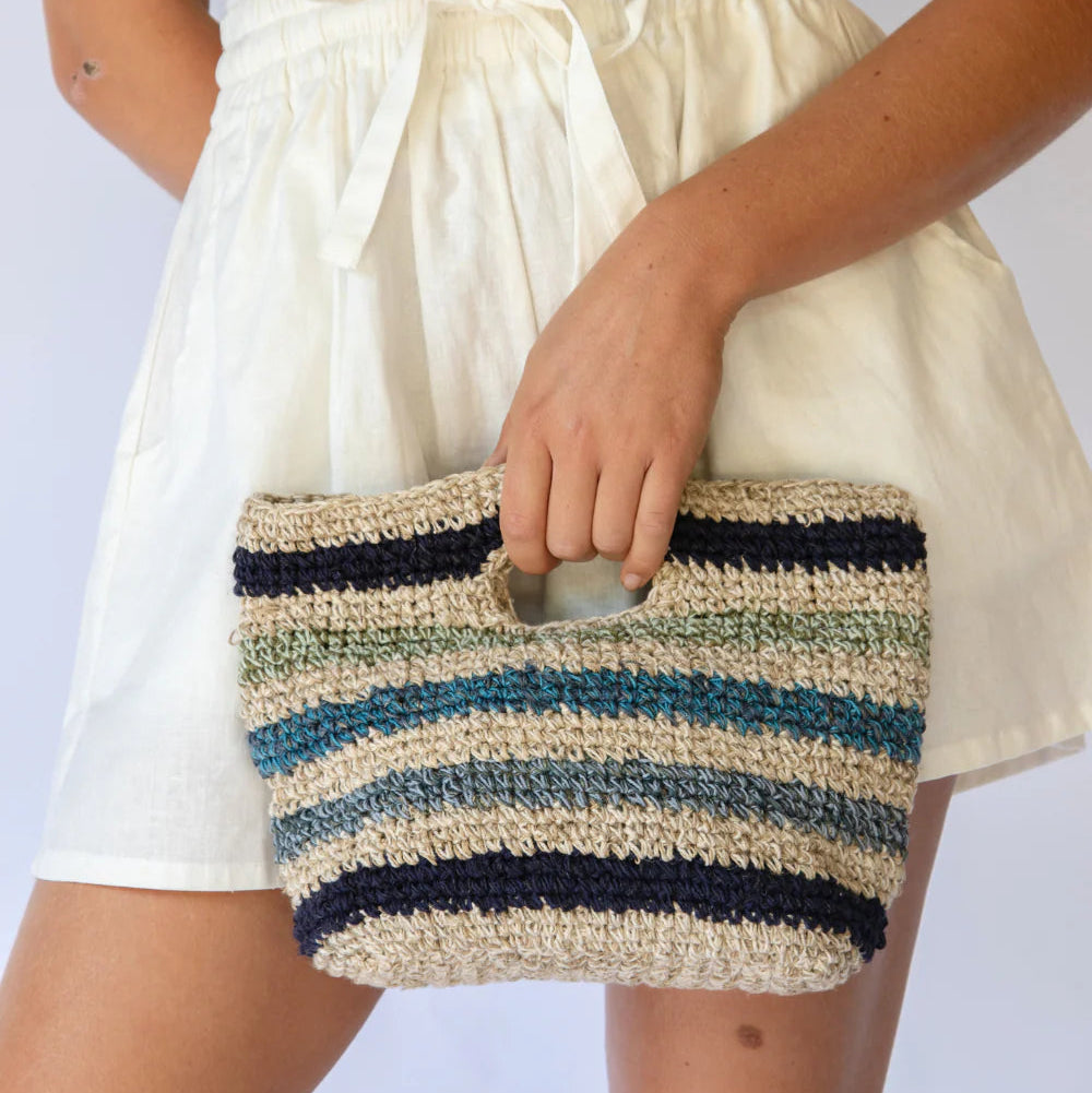 Person holding a striped woven clutch bag against a plain background