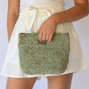 Person holding a green woven clutch with a plain background