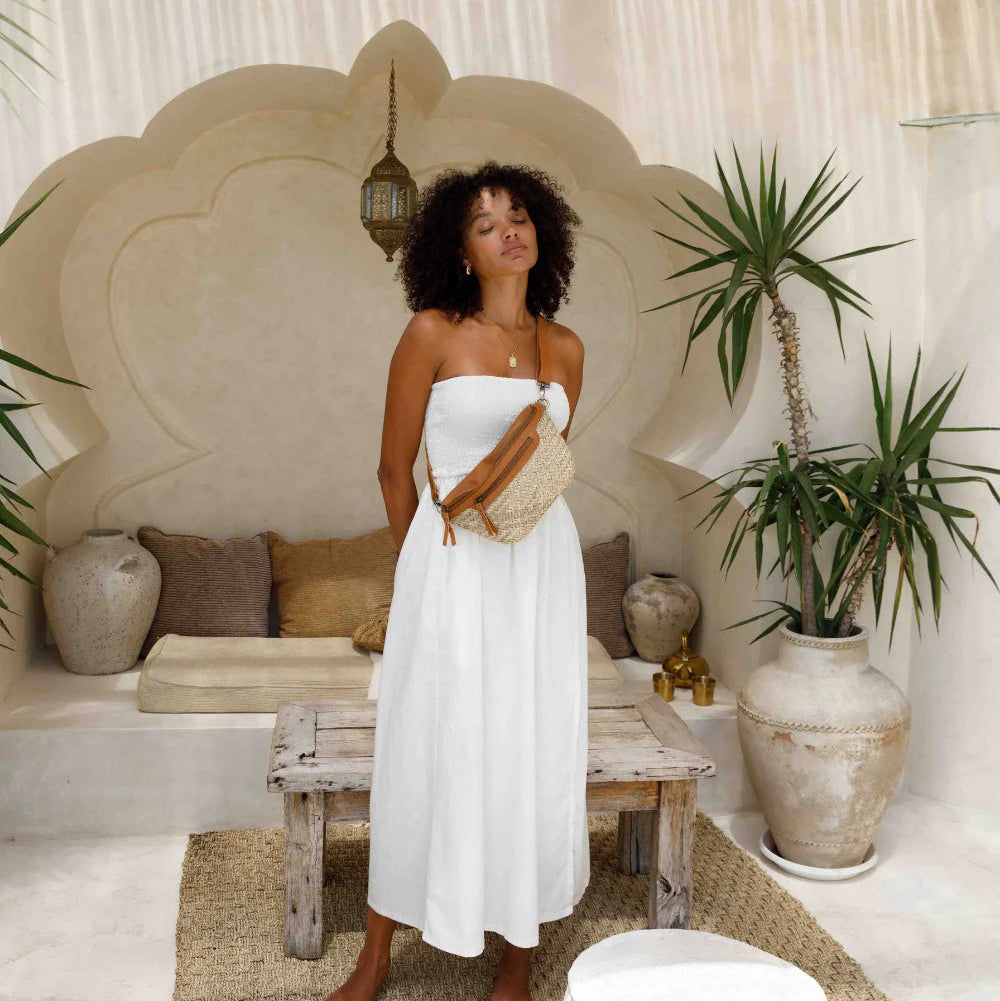 Woman in a white dress standing in a stylish indoor setting with plants and a wooden ceiling.