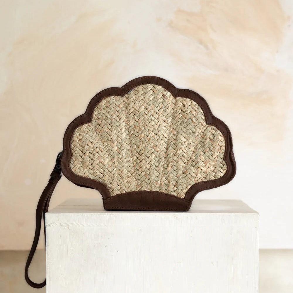 Shell-shaped clutch bag made of woven material on a white pedestal with a neutral background