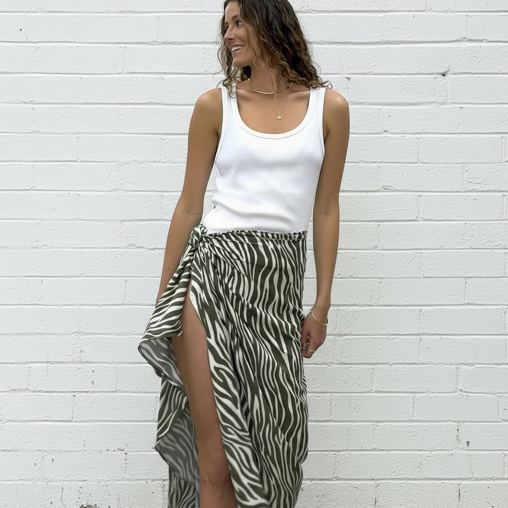 Woman wearing a white tank top and zebra print sarong in front of a white wall.