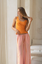 Load image into Gallery viewer, Woman wearing an orange tank top and striped pants in a softly lit room.
