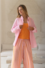 Load image into Gallery viewer, Woman wearing a pink shirt and orange striped pants in a room with a decorative wall.
