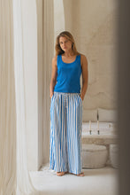 Load image into Gallery viewer, Woman wearing a blue tank top and striped pants standing in a room with architectural details.
