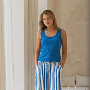 Woman wearing a blue tank top and striped pants standing in a room with architectural details.