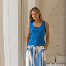 Load image into Gallery viewer, Woman wearing a blue tank top and striped pants standing in a room with architectural details.

