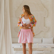Woman in colorful shirt and pink shorts standing in a stylish room with white decor.