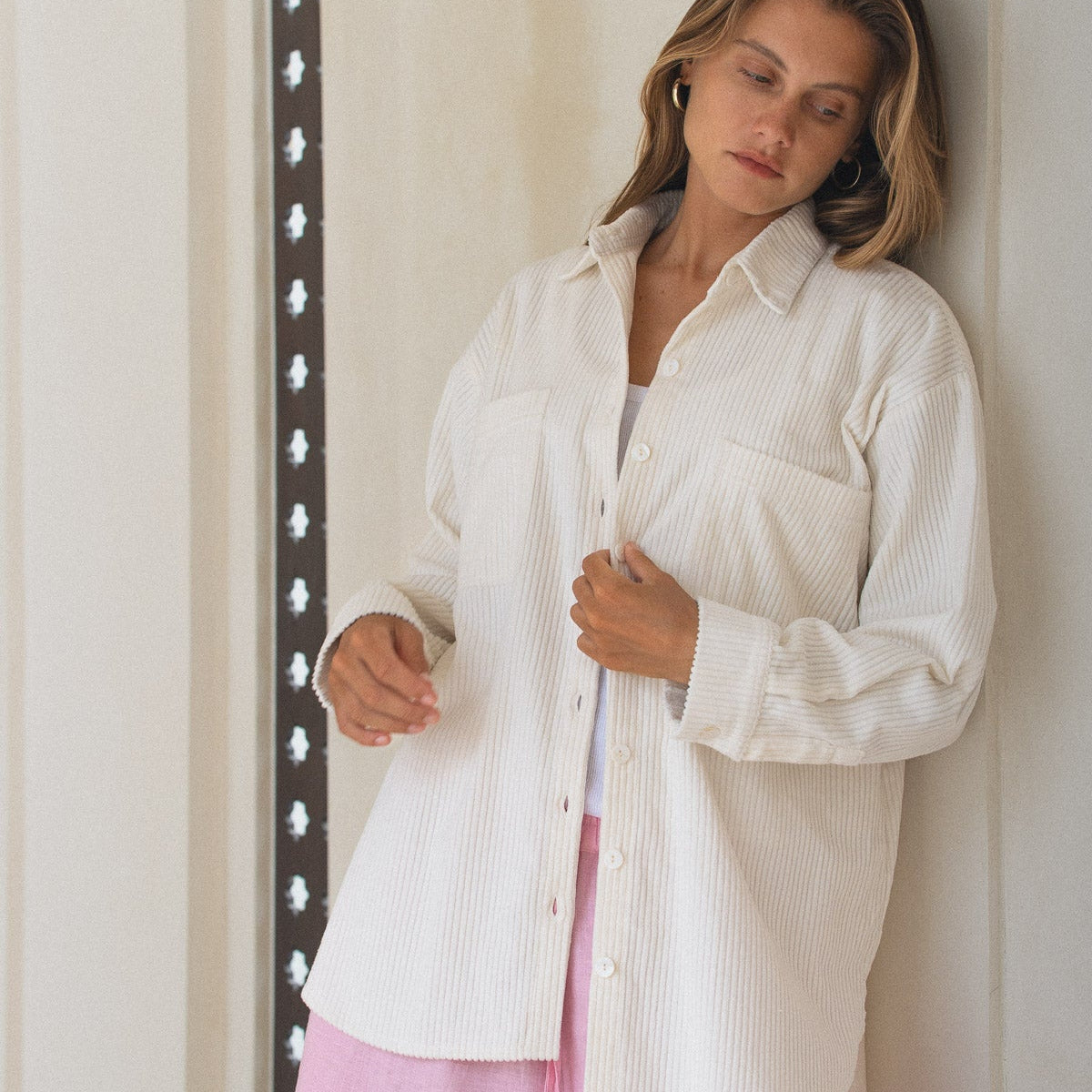 Woman wearing a white corduroy shirt and pink shorts against a neutral background
