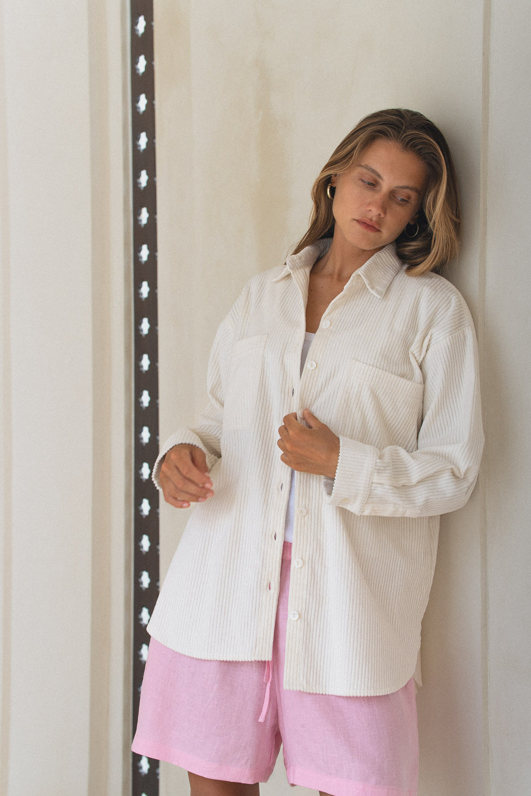 Woman wearing a white corduroy shirt and pink shorts against a neutral background