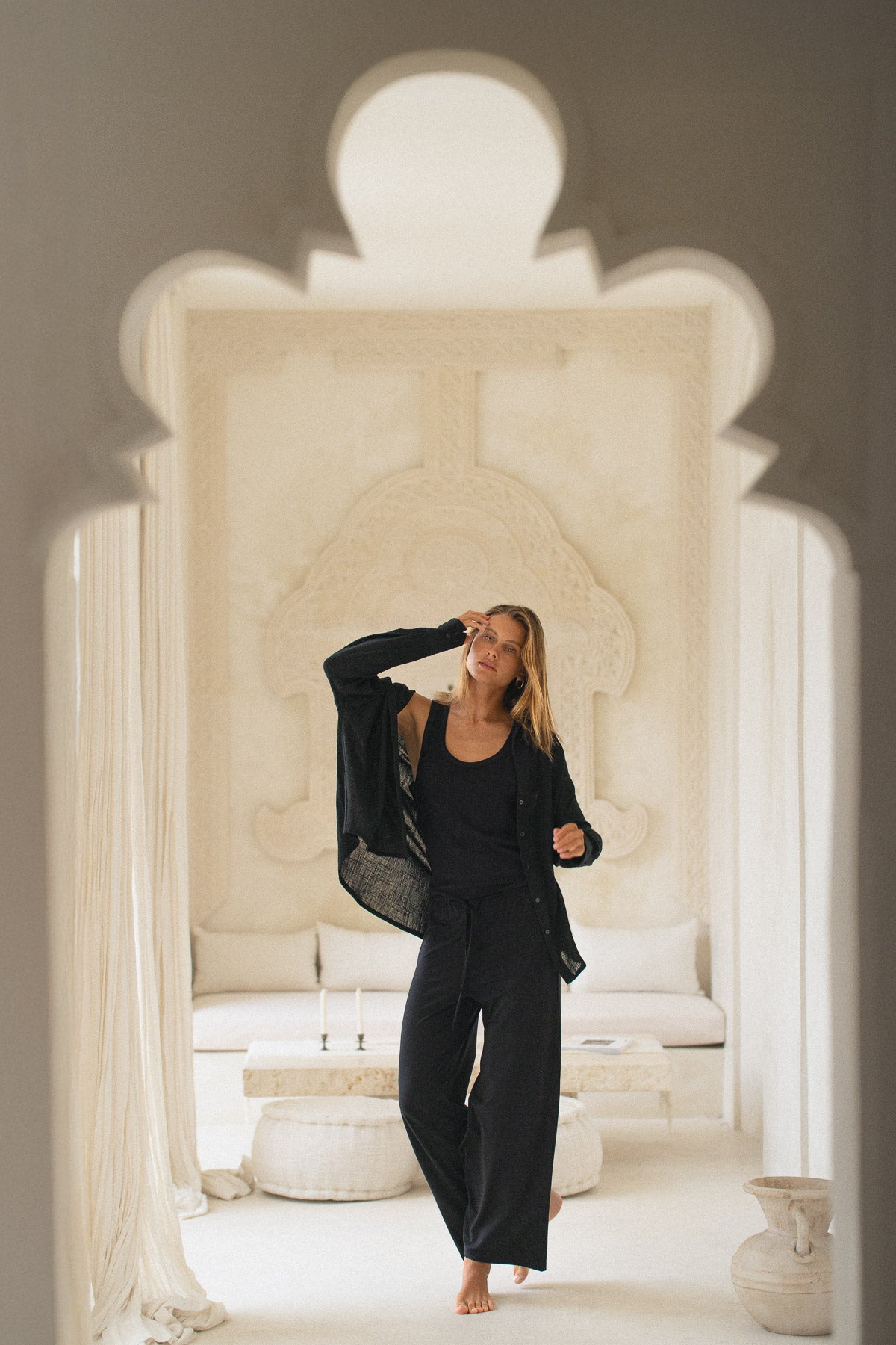 Woman in a black shirt, tank top and pants standing in a luxurious room with white decor