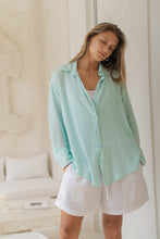 Load image into Gallery viewer, Woman in a light blue shirt , white tank top and white shorts standing in an elegant room
