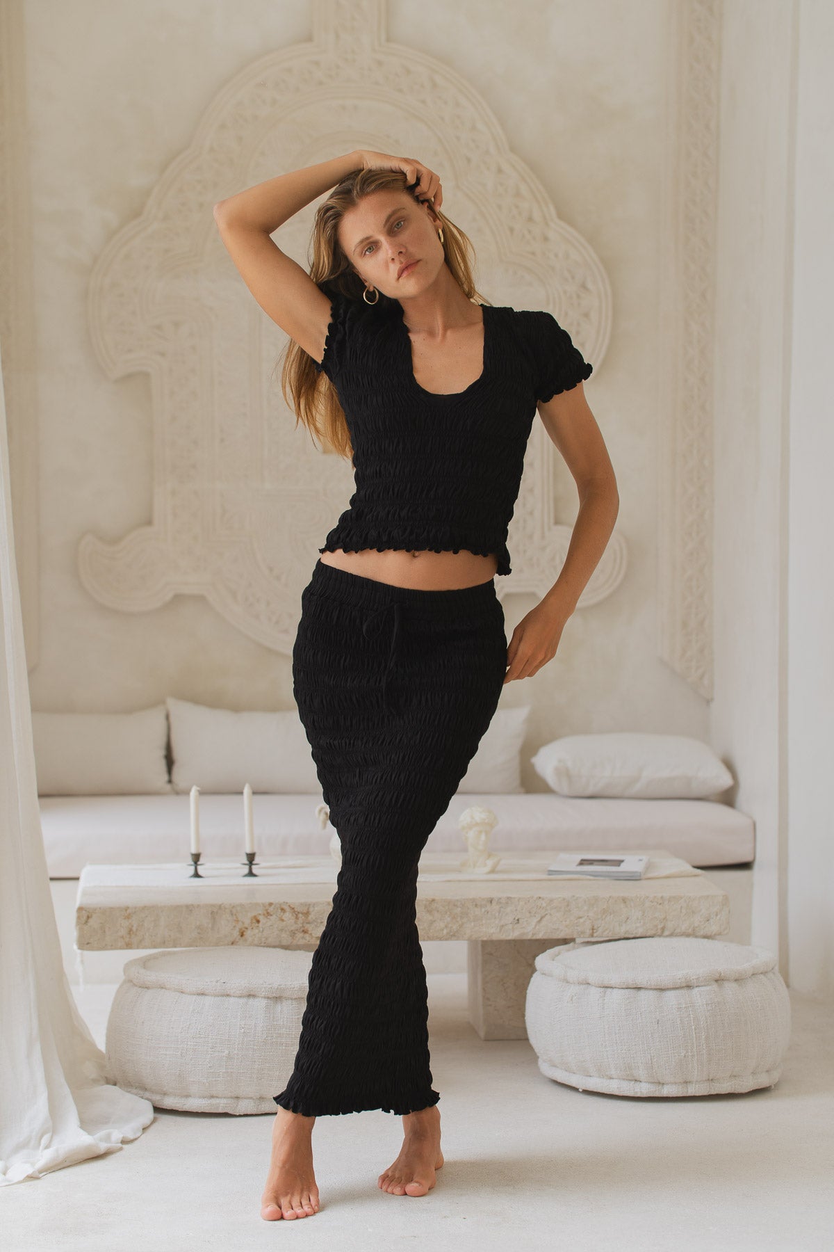 Woman in black shirred top and shirred maxi skirt standing in a minimalistic room with white decor