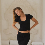 Woman in black shirred top and shirred maxi skirt standing in a stylish room with white decor