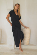 Load image into Gallery viewer, Woman wearing a black maxi dress leaning against a white wall with a large vase.
