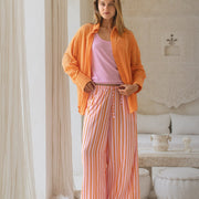 Woman wearing an orange jacket and striped pants in a room with decorative elements.