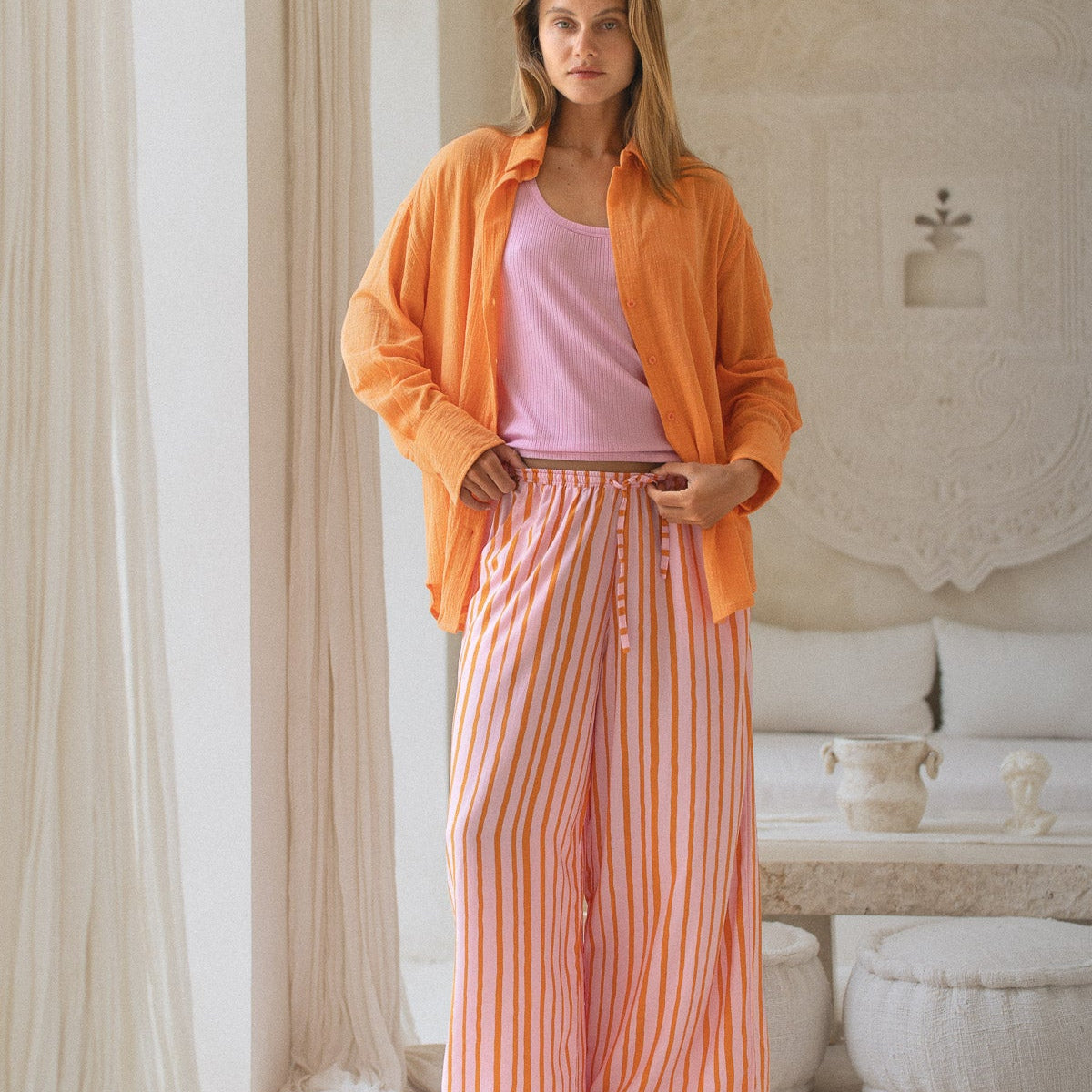 Woman wearing an orange jacket and striped pants in a room with decorative elements.