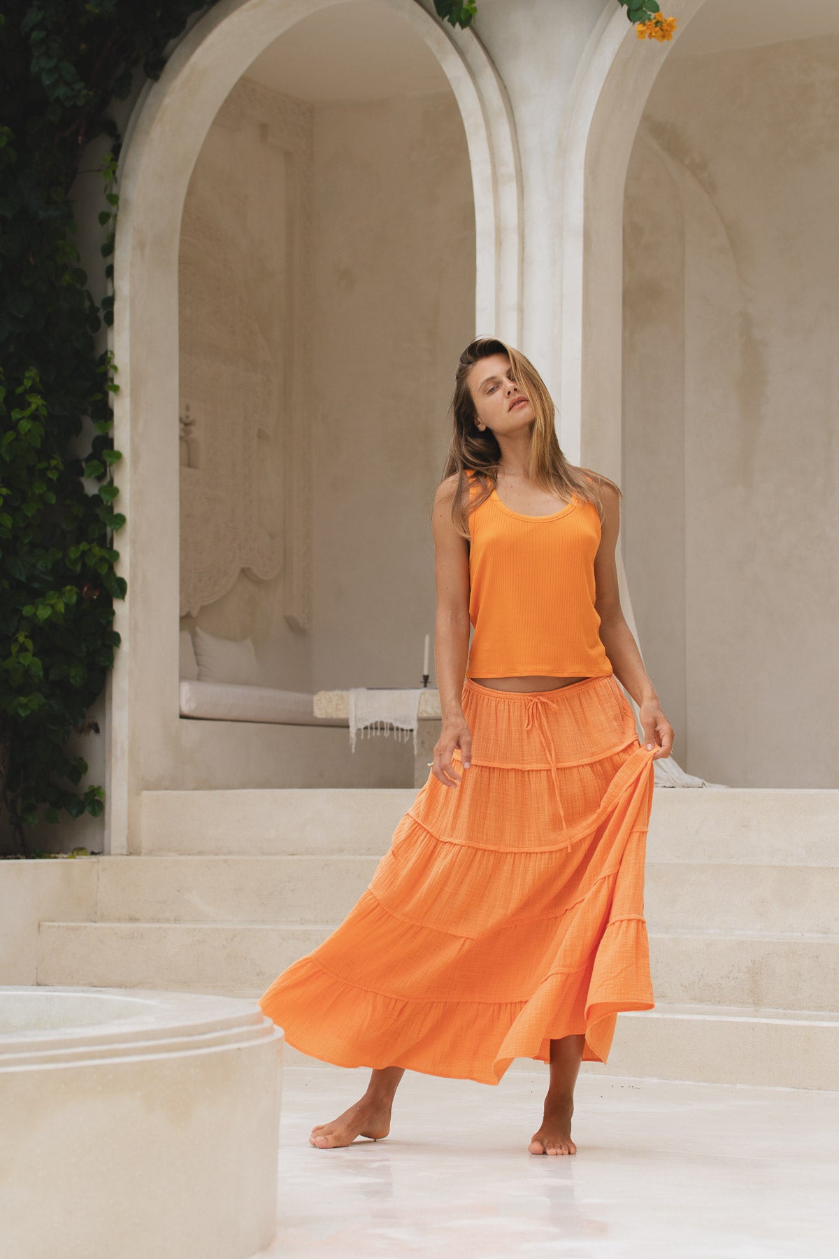 Woman in an orange skirt and tank top standing in front of a classical architectural archway.