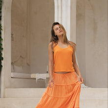 Load image into Gallery viewer, Woman in an orange tank top and skirt standing in front of classical architecture
