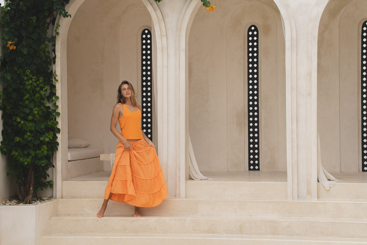 Woman in an orange skirt and tank top standing in front of a classical architectural archway.