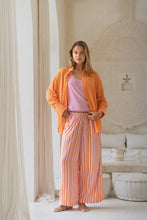 Load image into Gallery viewer, Woman wearing an orange shirt and pink striped pants in a bright room.

