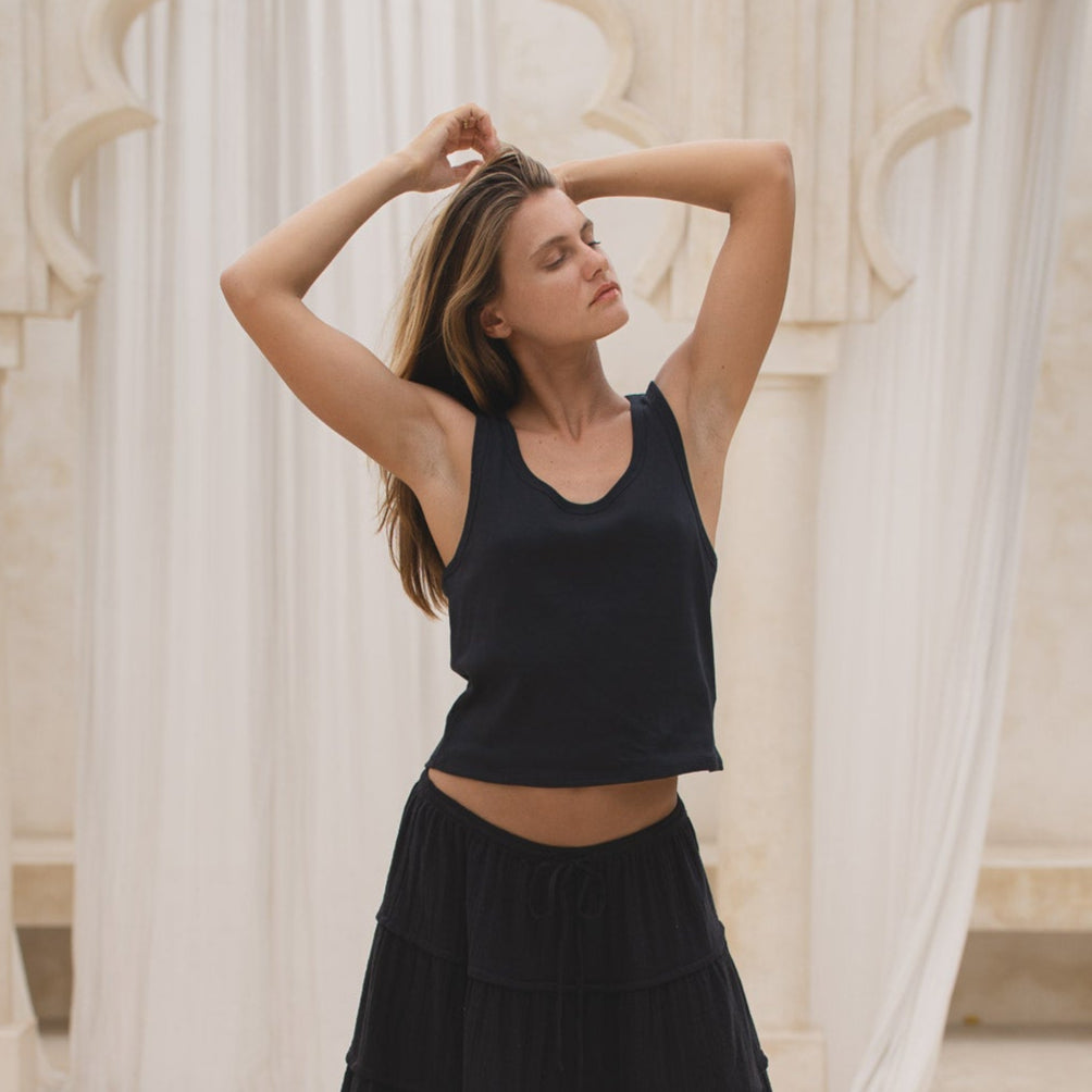 Woman in a black tank top and skirt  standing on steps with white columns in the background
