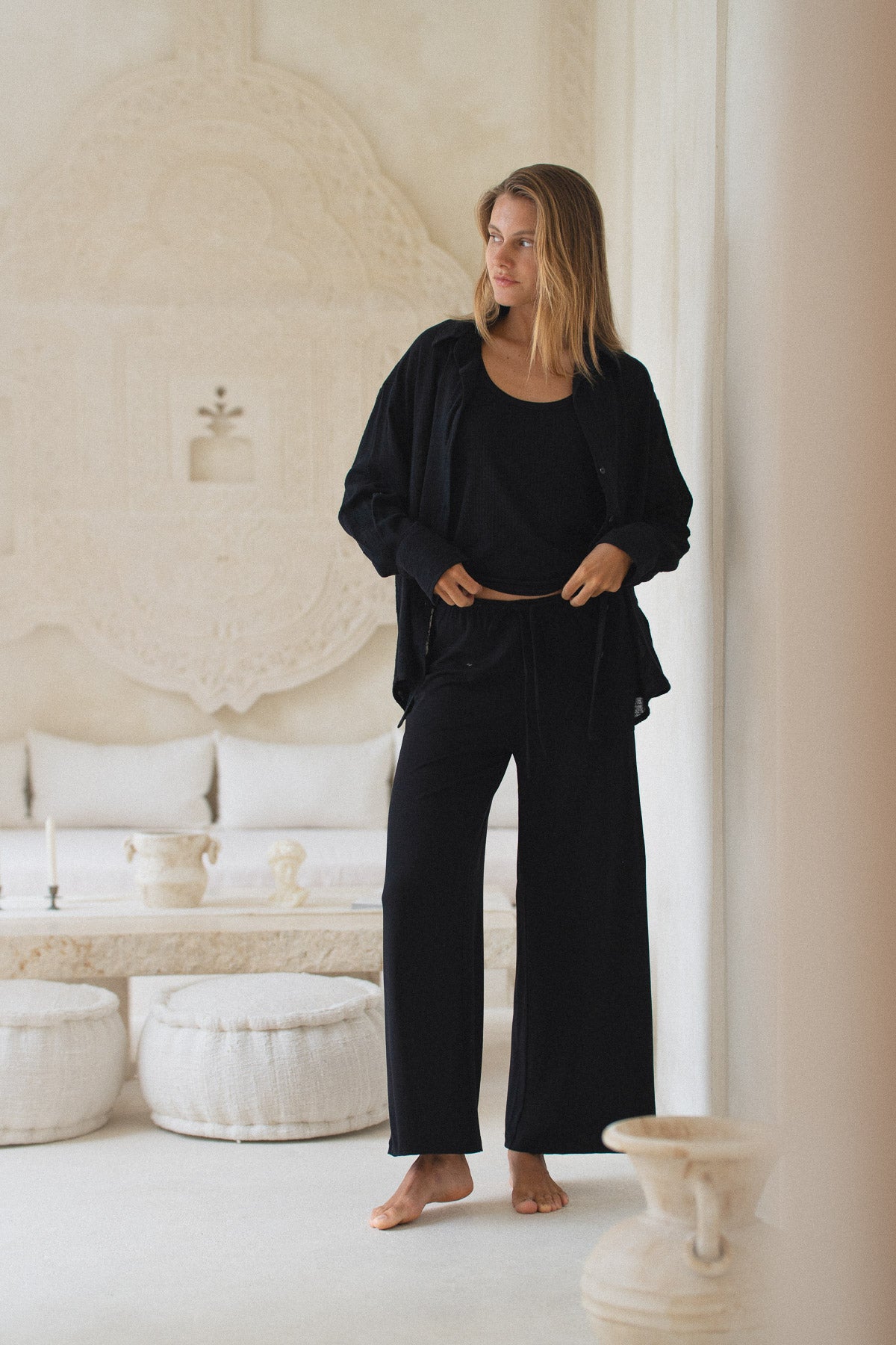 Woman in black outfit standing in a minimalistic room with white decor
