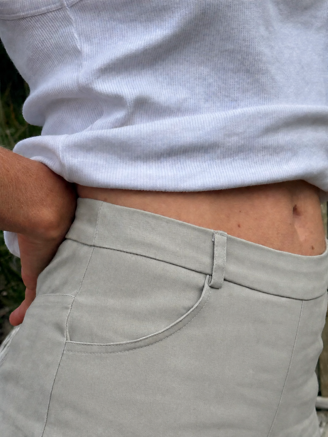 Close-up of a person wearing light gray trousers and a white ribbed top, with the waistband and front pocket of the pants visible.