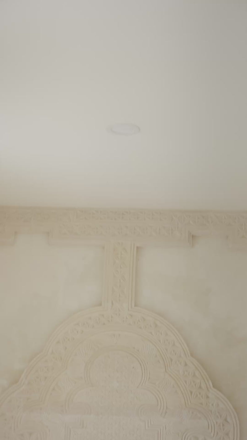 Woman wearing an orange shirt over a pink top and orange striped pants sitting on a daybed against a white wall.