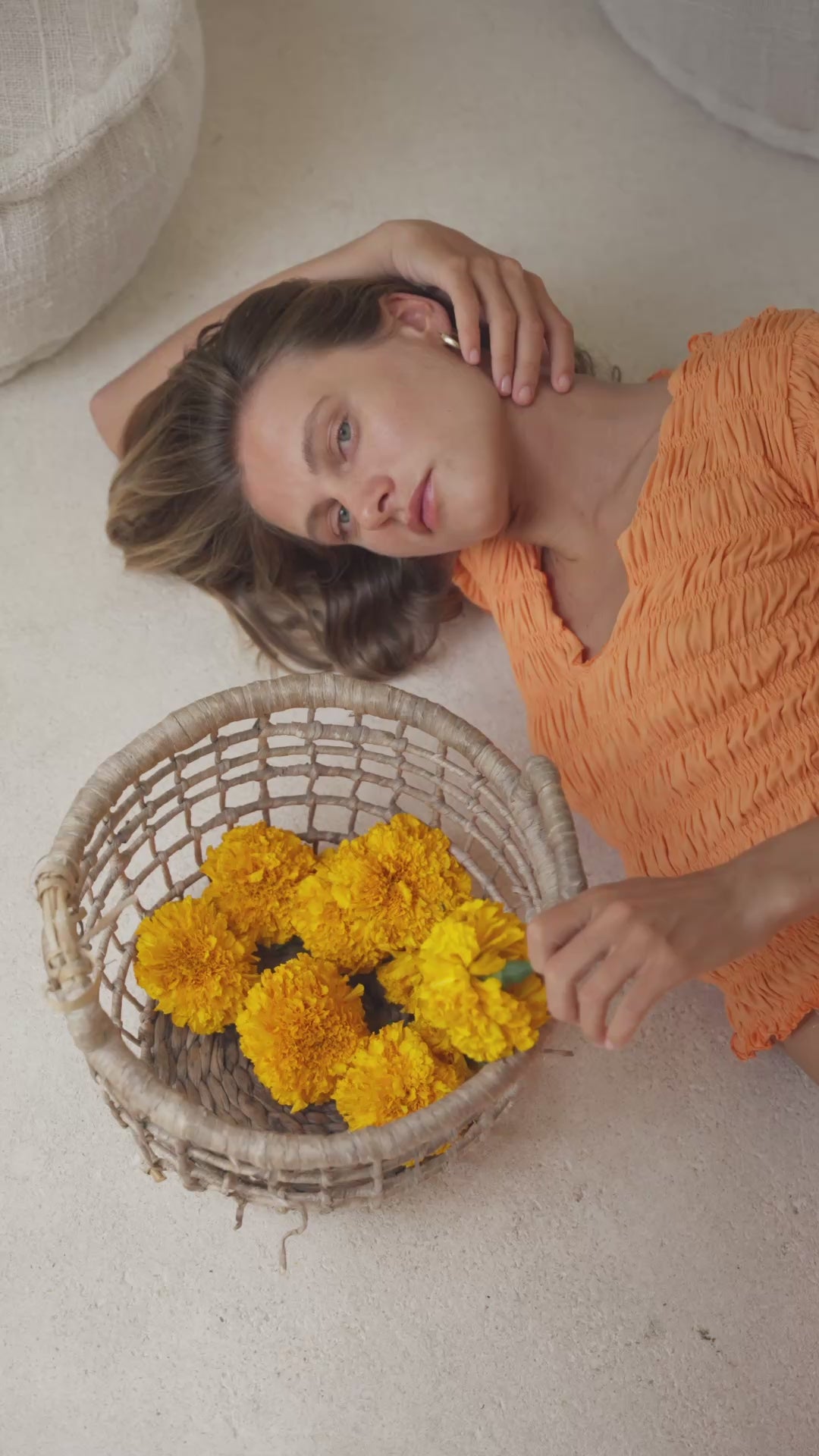 Load video: Woman in orange shirred top and maxi skirt lying on a daybed with intricate wall designs in the background