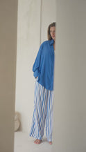 Load and play video in Gallery viewer, Woman standing by a  white wall wearing a blue shirt, white tank top, and striped pants.
