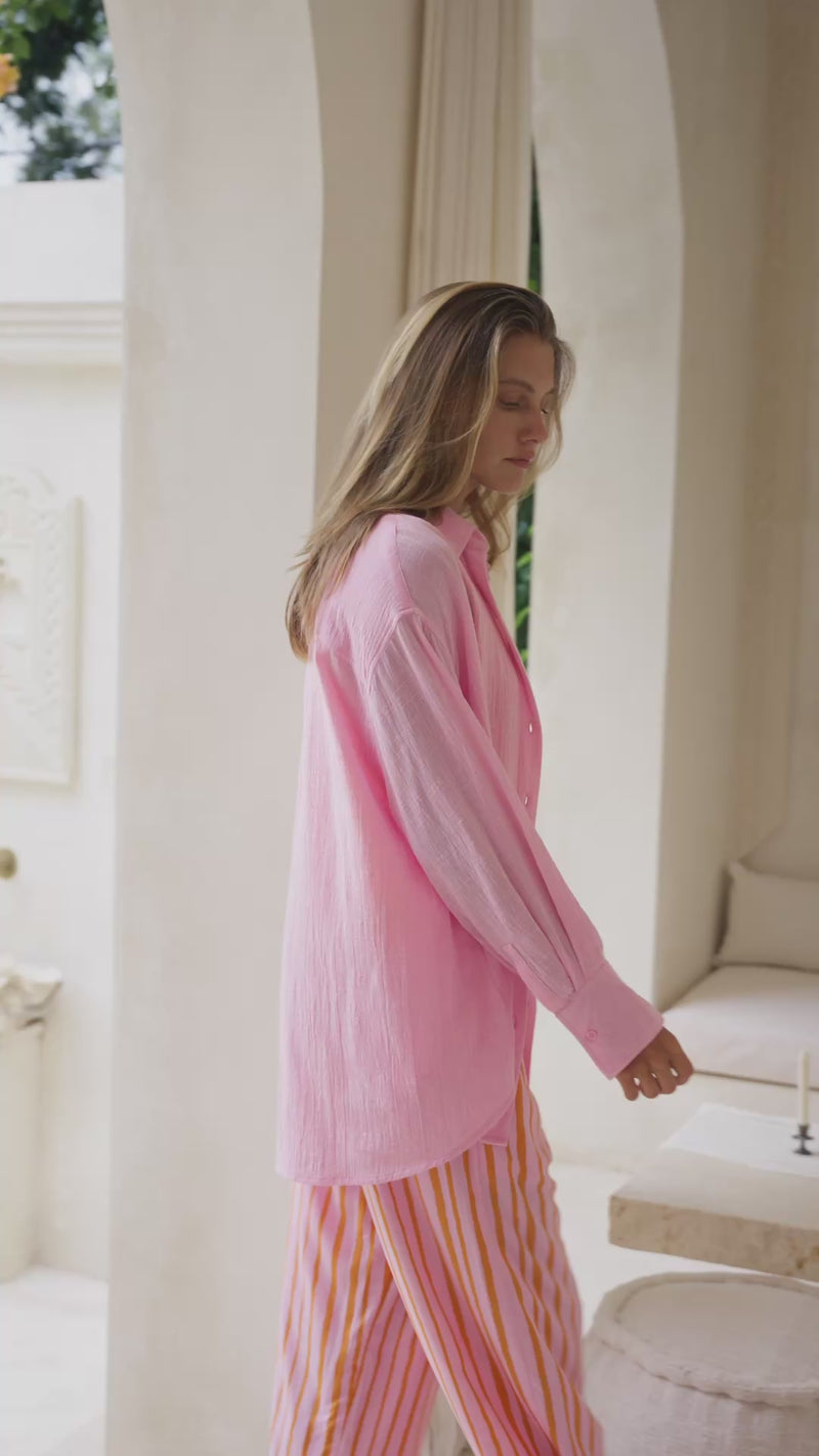 Woman wearing a pink shirt over an orange top and striped pants in a neutral setting