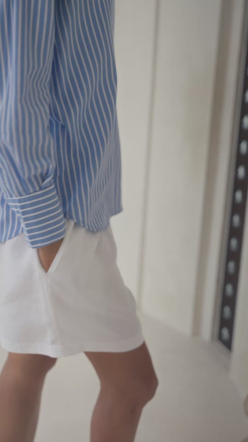 Woman in a blue striped shirt and white shorts in a stylish living room.
