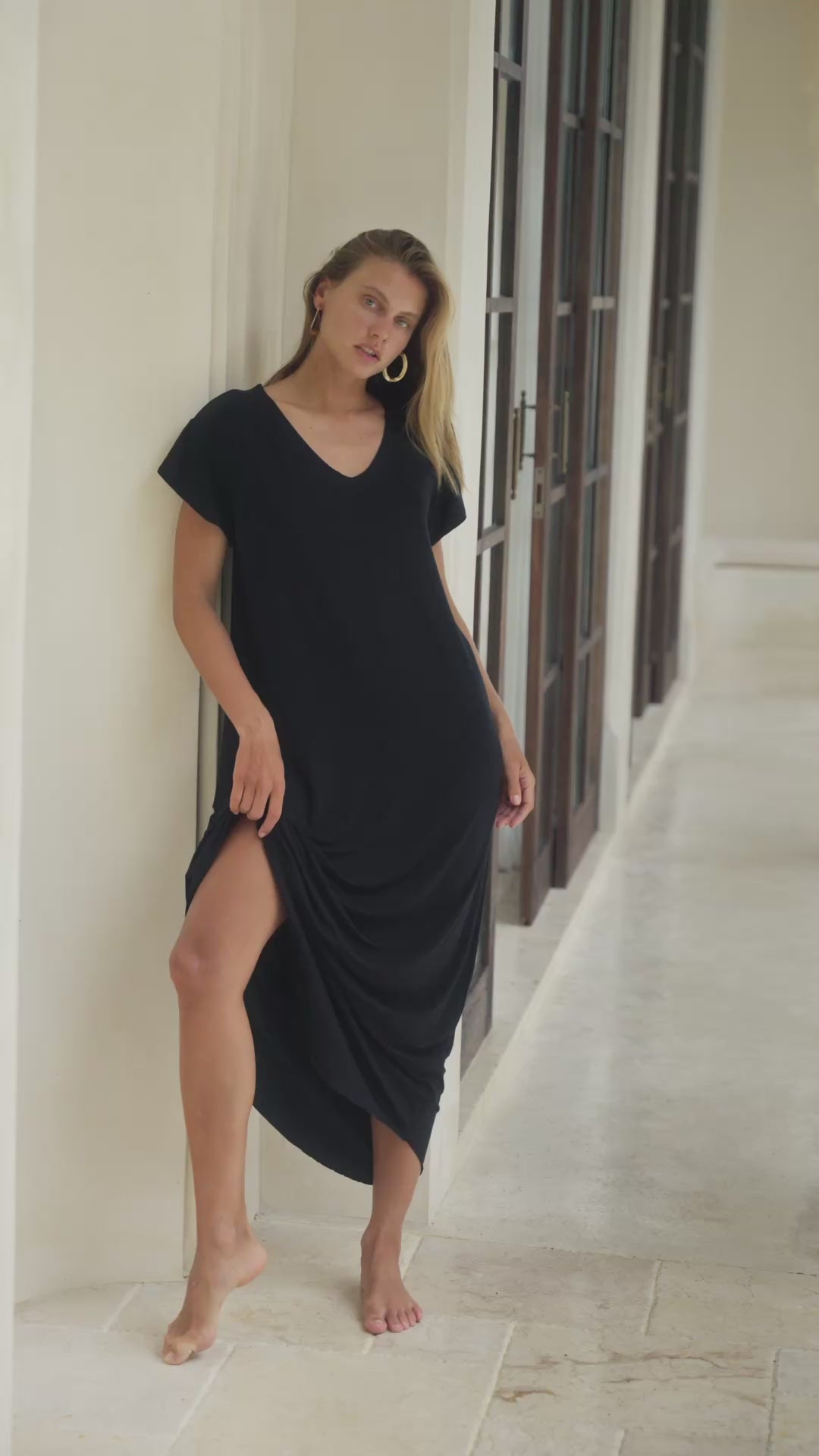 Load video: Woman in a black maxi dress standing  in a bright room.