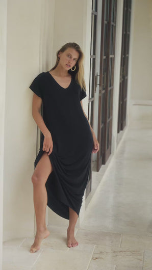 Woman in a black maxi dress standing  in a bright room.