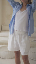 Load and play video in Gallery viewer, Woman in a blue striped shirt over a white tank top and white shorts standing in a stylish living room.
