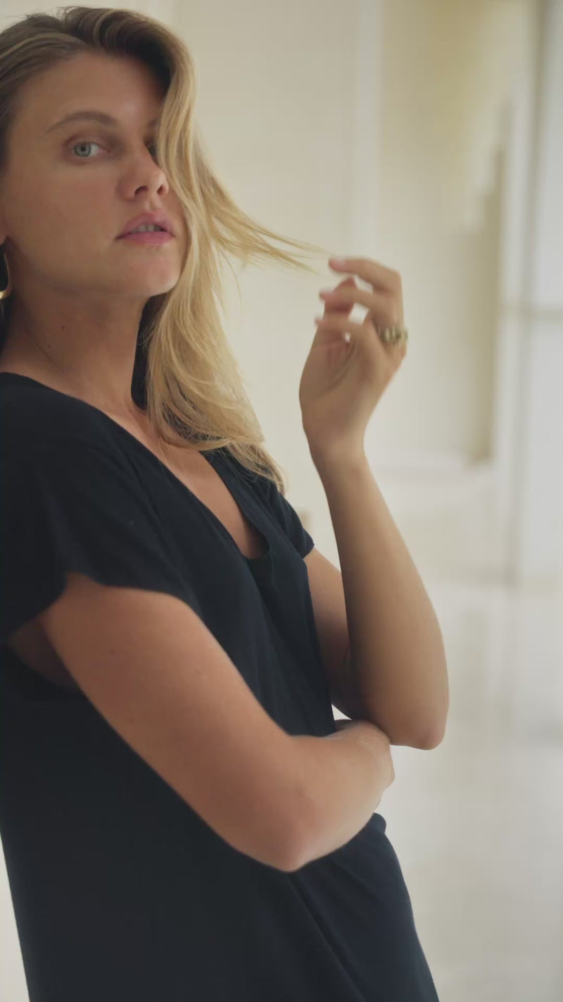 Woman in a black maxi dress standing in a bright room.