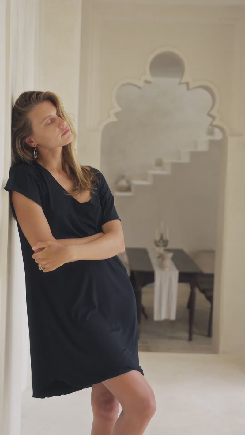 Woman wearing a black mini dress against a white curtain background