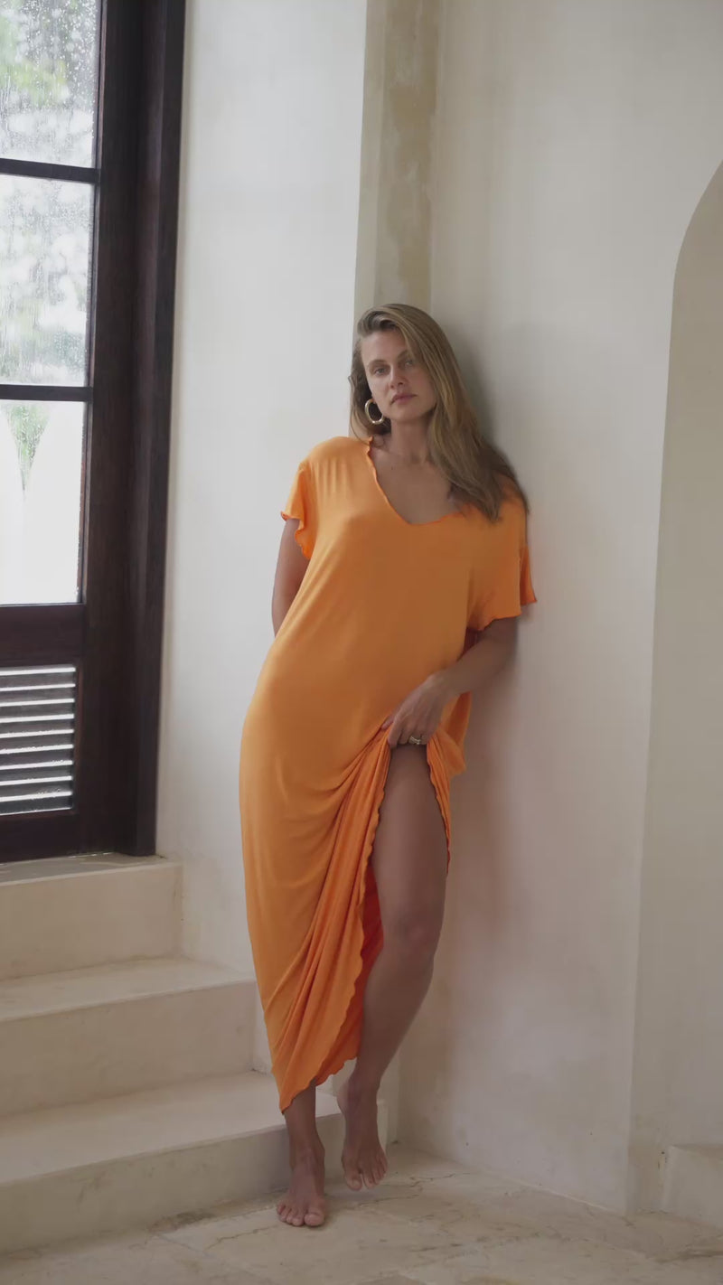 Woman in an orange maxi dress standing in a stylish room with white decor.