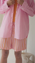 Load and play video in Gallery viewer, Woman wearing a pink corduroy shirt over an orange top and striped shorts, standing in a light and airy room

