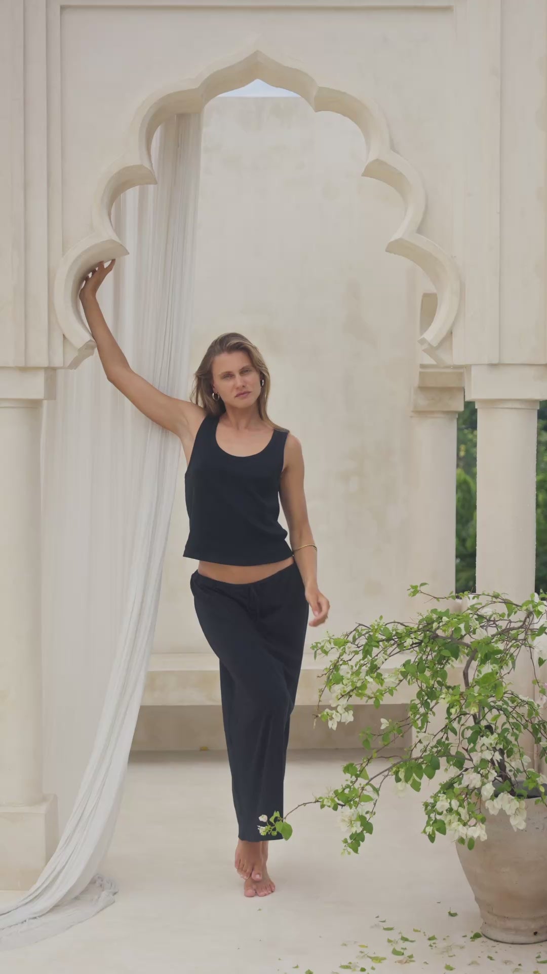 Load video: Woman wearing a black maxi skirt and tank top in a marble courtyard setting.