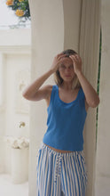 Load and play video in Gallery viewer, Woman wearing a blue tank top and striped pants standing in a room with architectural details.
